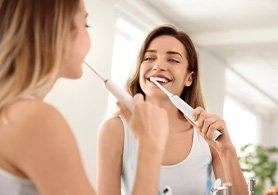 a woman brushing her teeth with an electric toothbrush