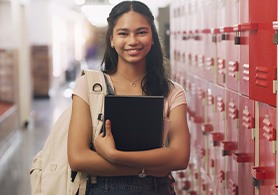 a high school student standing in front of lockers holding a notebook