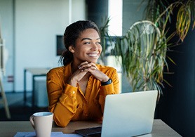 a smiling woman sitting at a table with her laptop out