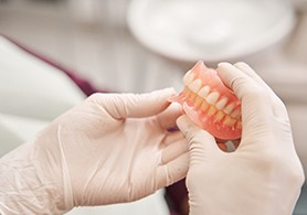 gloved hands holding dentures