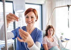 a woman in scrubs hooking up an IV for a patient sitting behind them