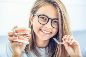 a teen holding braces in one hand and clear aligners in the other